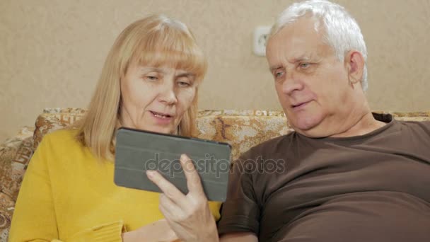 Літнім людям пару кільця на відео посилання на планшеті. Чоловік і дружина, сидячи у себе вдома на дивані. Концепція спілкування близькі родичі — стокове відео