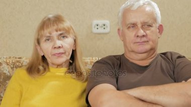 Yaşlı çift evde koltukta istirahat ve kameraya bakıyor.
