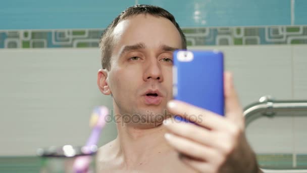 Joven hombre atractivo en el baño hace selfie habitación de hotel. Sonríe y cambia la postura. Sin camisetas con torso desnudo — Vídeos de Stock