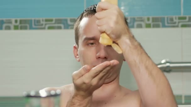 Ελκυστικός νεαρός επιχρίσματα μια κρέμα χεριών στο μπάνιο του δωματίου. Αυτός να χύνει η κρέμα και να τρίβει τα χέρια του. Αυτός φαίνεται στην κάμερα — Αρχείο Βίντεο