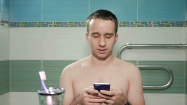 Otel odasının banyoda telefonda SMS yazma genç çekici bir adam. Çıplak bir gövde ile T-shirt olmadan mesaj telaffuz