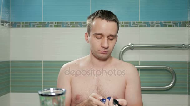 年轻有魅力的男人在浴室里剃须后使用的奶油。它是电动的刮胡子，把奶油放在脸上。他在刺激皮肤摩擦双手 — 图库视频影像