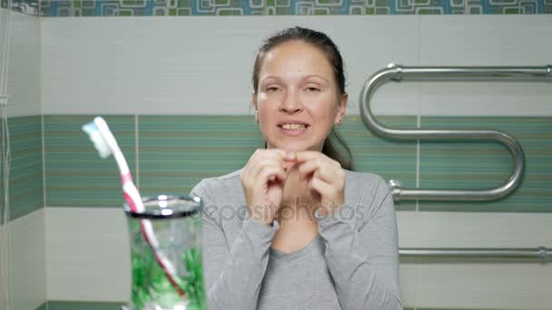 Jonge aantrekkelijke vrouw gebruik tandzijde in de badkamer van de hotelkamer. Ze zorgvuldig chitit gaten tussen de tanden en controleer het resultaat aan het eind — Stockvideo