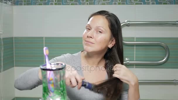 Jonge aantrekkelijke vrouw haar haren in de badkamer te poetsen. Ze gooit de lange haren van de ene kant naar de andere, en kijkend naar de camera. — Stockvideo