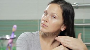 Genç çekici kadın banyoda saçları fırçalama. O uzun saçlı bir taraftan diğer ve kamera seyir atar.