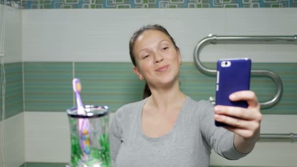 Молода приваблива жінка робить селфі-телефон у ванній кімнаті готелю. Вона посміхається і змінює поставу на краще фото — стокове відео