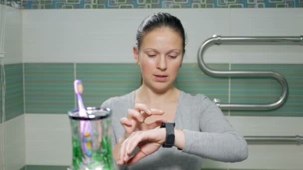 Giovane donna attraente controlla i messaggi sull'orologio intelligente nel bagno della camera d'albergo. Sorride dettando un messaggio vocale in risposta — Video Stock