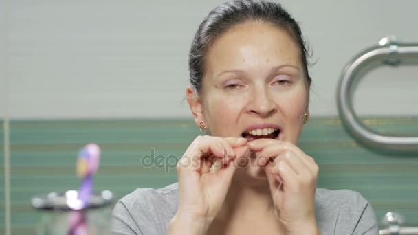 Молода приваблива жінка використовує зубну нитку у ванній кімнаті готелю. Вона обережно чіпляє отвори між зубами і перевіряє результат в кінці — стокове відео