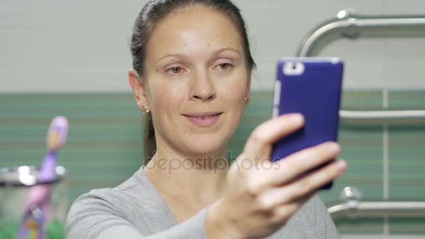Jovem mulher atraente fazendo telefone selfie no banheiro do quarto de hotel. Ela sorri e muda a postura para uma foto melhor — Vídeo de Stock