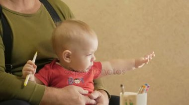 Çekici bebek işaretçileri olan dedesi ile kağıt üzerinde çizim. Dedesi eve kucağında oturan bir çocuk. Çocuk 1 yıl.