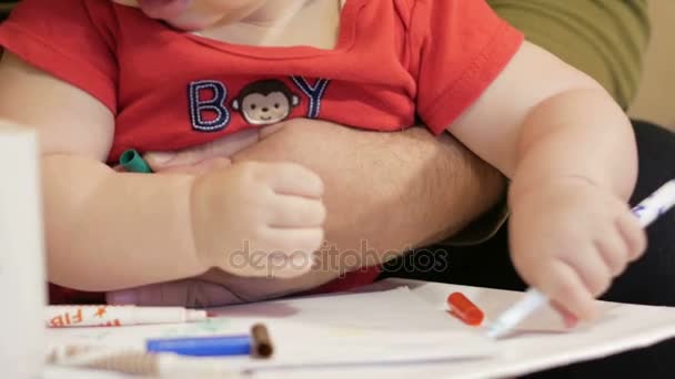 Attractive baby drawing with markers on paper with his grandfather. A boy sitting on his lap in the house his granddad. Kid 1 year. — Stock Video