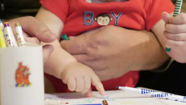 Attraktiva baby ritning med markörer på papper med sin farfar. En pojke som sitter i hans knä i huset hans farfar. Barn 1 år. — Stockvideo