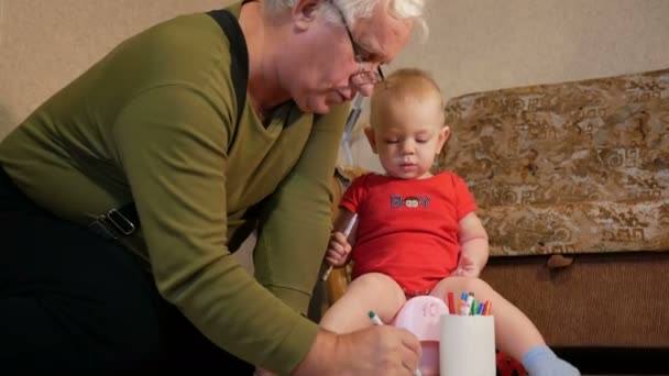 Attraktive Baby sitzt auf dem Topf und zeichnet mit ihrem Großvater Marker auf Papier. Der Junge pinkelt und spielt mit der Familie zu Hause. Kind 1 Jahr. — Stockvideo