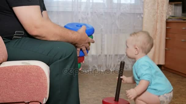 Attraente bambino che gioca con i nonni in una piramide. Sta cercando di raccogliere un giocattolo da un nonno — Video Stock