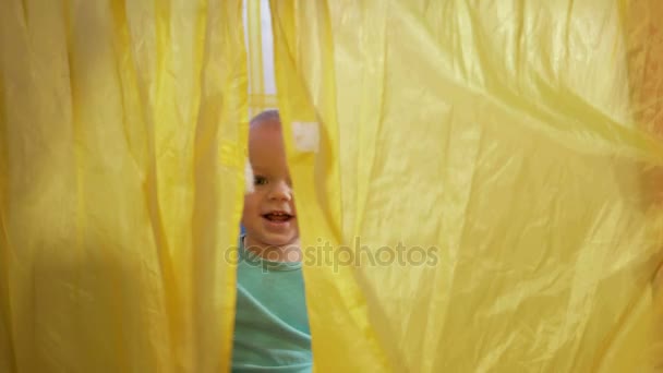 Aantrekkelijke baby spelen in de kleurrijke tent van kinderen in het huis. De jongen wordt geopend de gordijnen, hoezen en lachen om de camera — Stockvideo