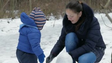Çekici anne ve bebek sculpts kış ormandaki küçük kardan adam. Noel tatili için aile eğlence
