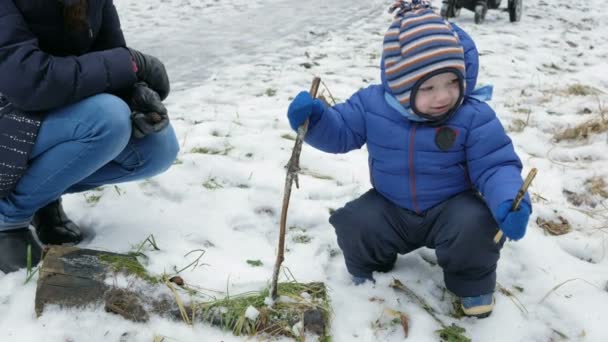 Приваблива дитина грає з матір'ю взимку на вулиці. Хлопчик в руках гілок дерев — стокове відео