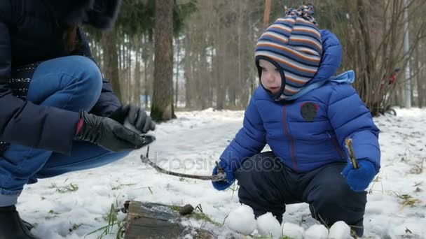 森の中での外の冬で母と遊んで魅力的な赤ちゃん。雪玉を母用金歳少年 — ストック動画