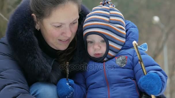 Attraktiva mor och baby skulpterar liten snögubbe i skogen vinter. Familjen roligt för jullovet — Stockvideo