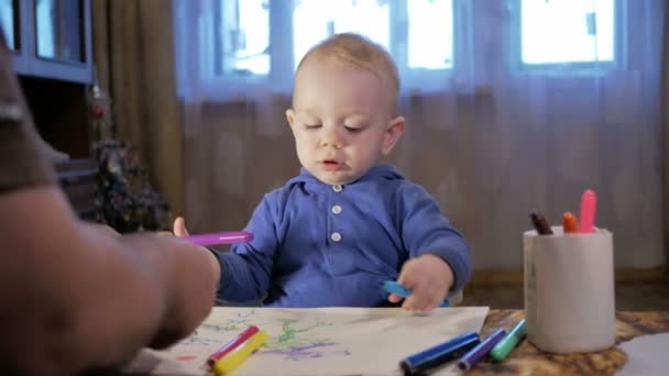 彼の子供の孫の祖父は、紙にマーカーを描画します。少年は、慎重に見えるし、助けます。驚きと笑顔。家庭での子供の教育の概念 — ストック動画