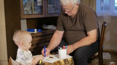 Dedesi onun torunu çocukla işaretleri kağıt üzerinde çizer. Çocuk dikkatle bakar ve yardım. Gülümseyen ve sürpriz. Öğretim çocuklar evde kavramının