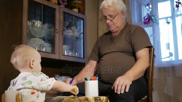 Grandfather with his grandson kid draws markers on paper. The boy looks carefully and help. Smiling and surprised. The concept of teaching children at home — Stock Video