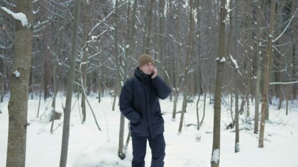 Un giovane va in una foresta invernale e parla al telefono. Si ferma e finisce la conversazione. Un uomo con una giacca scura e un cappello caldo . — Video Stock