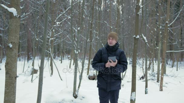 若い男は、雪の中で冬の森に行くし、タブレット上指向です。彼は電子地図で右方向を探してください。. — ストック動画