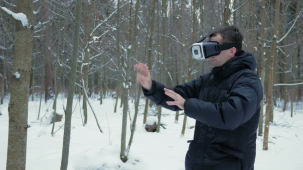 Kışın karlı bir ormanda bir sanal gerçeklik kulaklık giyen bir adam. Sanal nesneleri dokunmak çalışır. Sıcak bir ceket giymiş ve kollarını sallayarak bir adam. — Stok video