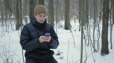 Karlı kış ormandaki telefonda sms mesajý yazmaya genç adam. O gülümser ve yazılı konuşuyor.