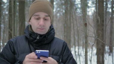 Karlı kış ormandaki telefonda sms mesajý yazmaya genç adam. O gülümser ve yazılı konuşuyor.