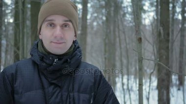 Kamera ve kış ormanda gülümseyen genç adam görünüyor. Karlı manzara. Bir adam bir koyu renk ceketli ve sıcak bir şapka.