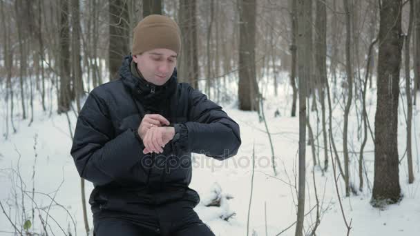 남자 겨울 눈 덮인 숲에서 스마트 시계에 메시지를 확인합니다. 그는 시계에 대 한 음성 응답을 지시 한다. 어두운 따뜻한 재킷을 입은 남자. — 비디오