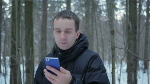 The young man goes in the winter forest and is oriented over the phone. He is looking for the right direction on the electronic map. — Stock Video