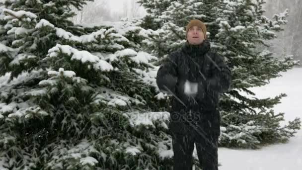 若い男は、カメラと冬の森で笑顔に見えます。大きな降雪。雪で遊んでいます。暗いジャケット、暖かい帽子の男. — ストック動画