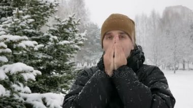 Genç bir adam kışın Ladin yakınındaki ormanda soğuktur. Büyük kar yağışı. Ellerinin üstünde nefes hes losyonları ve bir kukuleta ile eldiven giyer. Karlı manzara. Kameraya bakıyor