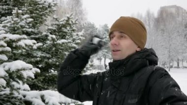 Genç adam, arayan bir kamera ve iskambil ile kış ormanda kar. Kartopu ve bunları atma Kış eğlence kavramı