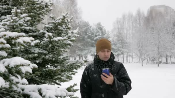 年轻人在雪地里的冬天森林里去，是面向通过电话。他正在寻找正确的方向在电子地图上。一个人在一件黑夹克和温暖罩. — 图库视频影像