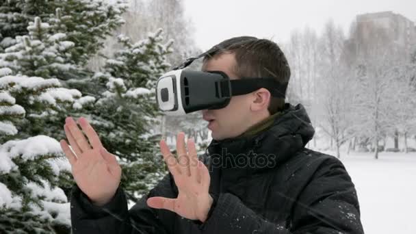 En man klädd i en virtuell verklighet headset på vintern i en snöig skog. Stora snöfall. Han försöker röra virtuella objekt. En man klädd i en varm jacka och vifta med armarna. — Stockvideo