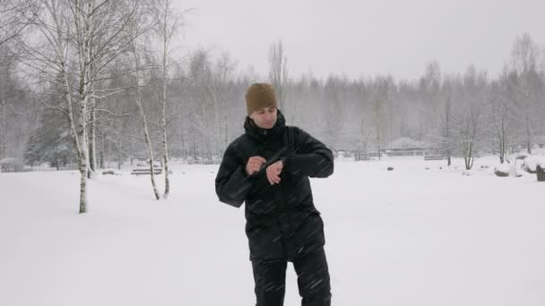 Een man controleert de berichten op de smart watch in het winter besneeuwde forest. Grote sneeuwval. Hij dicteert een reactie van de stem op de klok. Een man gekleed in een donkere warme jas. — Stockvideo