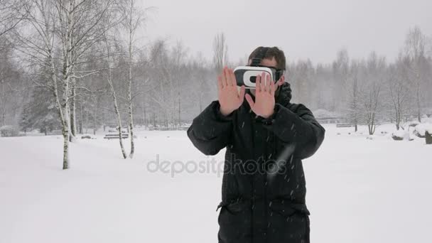 Kışın karlı bir ormanda bir sanal gerçeklik kulaklık giyen bir adam. Büyük kar yağışı. Sanal nesneleri dokunmak çalışır. Sıcak bir ceket giymiş ve kollarını sallayarak bir adam. — Stok video
