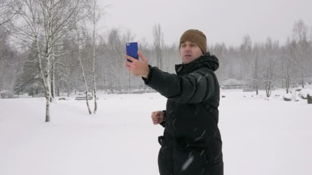男人在一个下雪的冬天森林使自拍照手机。他微笑着，变化的姿态更好的照片。可用性概念照片 — 图库视频影像