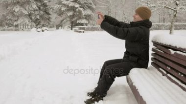 Karlı bir kış parkta selfie telefon kılıyor. O gülümser ve duruş daha iyi bir fotoğraf için değiştirir. kullanılabilirlik konsept fotoğraf