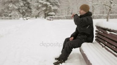 Bir adam akıllı izlemek karlı kış parkta iletilerini denetler. Sesli yanıt saat belirler. Karanlık bir sıcak ceket giymiş bir adam.