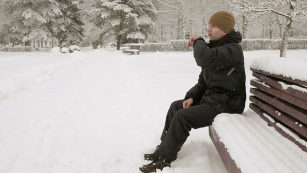 一个人在检查在多雪的冬季公园的智能手表上的消息。他口授的时钟的声音回应。一个人穿着黑色的小棉袄. — 图库视频影像