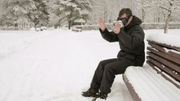 在一个下雪的公园在冬天戴着虚拟现实耳机一个人。他试图触摸虚拟对象。一个男人穿着一件温暖的外套，挥舞双臂，. — 图库视频影像