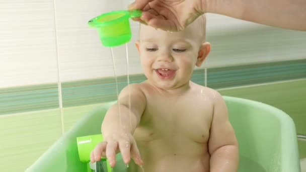 Madre bañando a un bebé atractivo. El niño está sonriendo y jugando con juguetes coloridos y agua. Chico durante un año. — Vídeo de stock