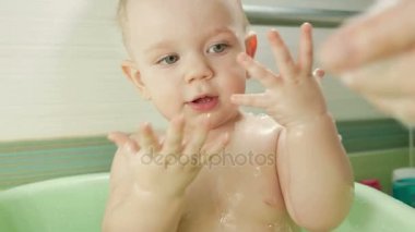 Mutlu bebek banyo köpük kabarcıkları ile oynarken. Anne küçük çocuk yıkama. Genç çocuk bir küvet içinde. Banyo oyuncakları ile gülümseyen çocuklar. Anne-baba ve çocuk su ile oynamak.