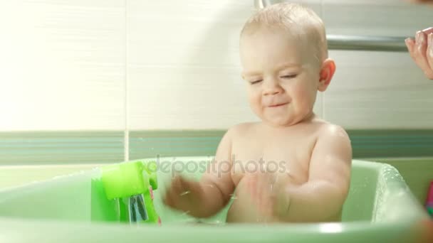 風呂に入って泡泡と遊ぶ幸せな赤ちゃん。母は少年を洗浄します。バスタブには若い子。おもちゃ付きのバスルームで子供たちを笑っています。親と子供が水と遊ぶ. — ストック動画