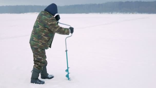 Pesca de inverno no rio. Um homem faz um buraco no gelo . — Vídeo de Stock